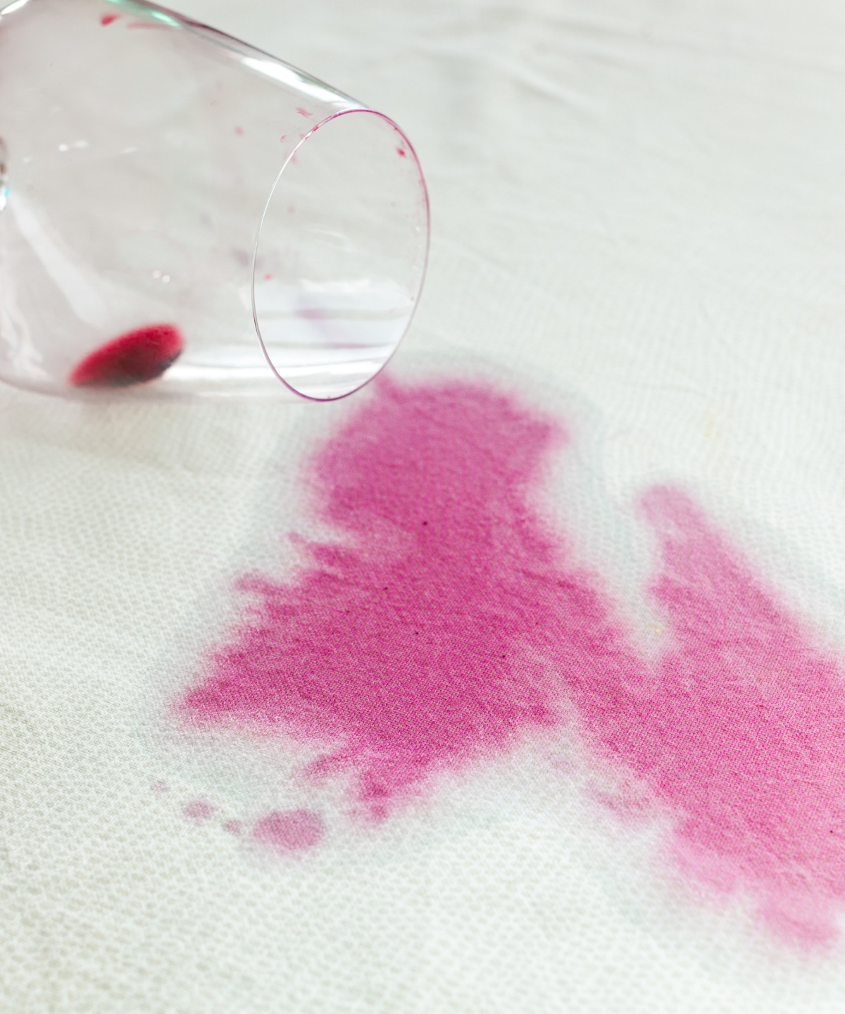 Ein umgefallenes Glas Rotwein hinterlässt einen Fleck auf einem weißen Stoff.
