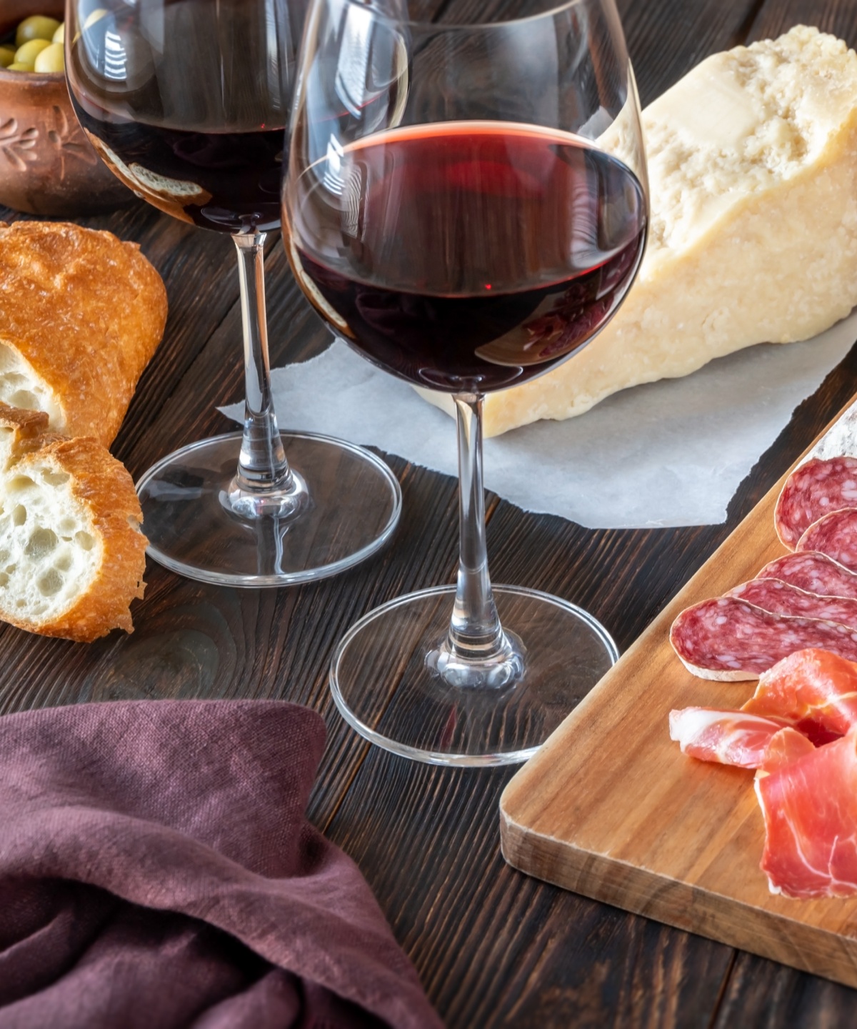 Rotwein im Glas, Schinken, Salami, Käse und Brot auf einem Holztisch, serviert für eine Pfälzer Brotzeit.