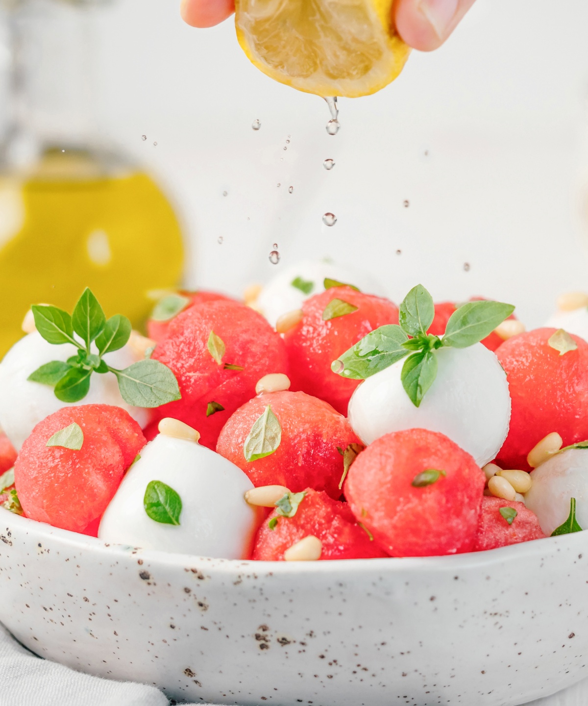 Ein Melonen Mozzarella Salat, garniert mit Pinienkernen und Basilikum, wird mit frisch gepresster Zitrone übergossen