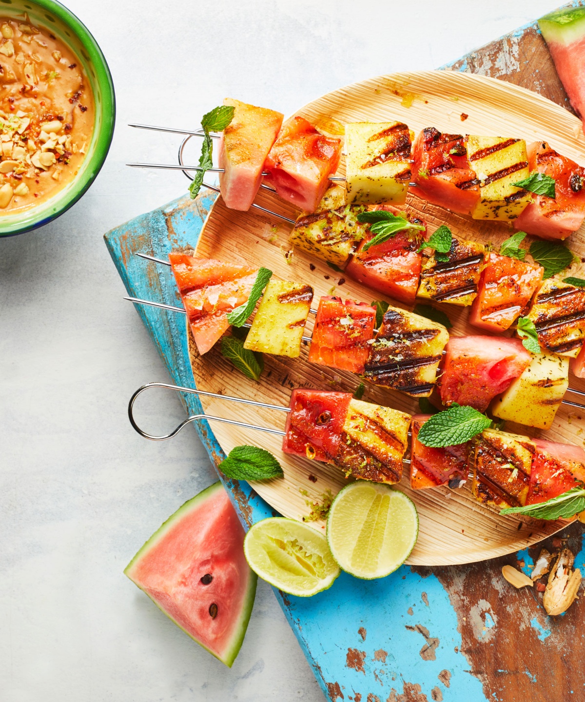 Fertige Grillspieße mit Wassermelone und Räuchertofu liegen auf einem Holzteller, dazu steht ein feiner Dip bereit