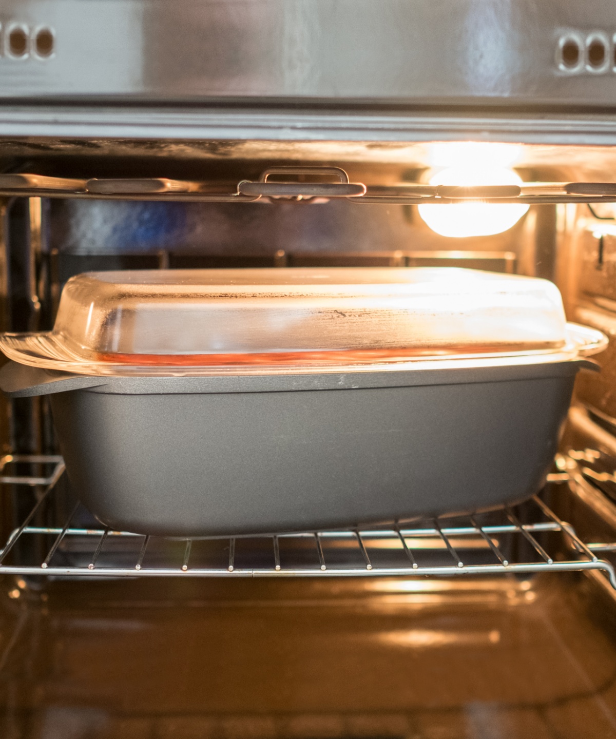 Eine graue Auflaufform mit gläsernem Deckel im Backofen.