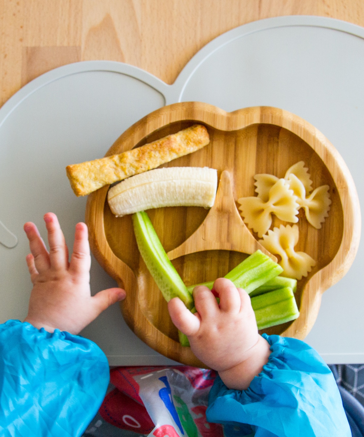 Ein Kleinkind isst Salatgurkenstreifen, Banane und Nudeln.