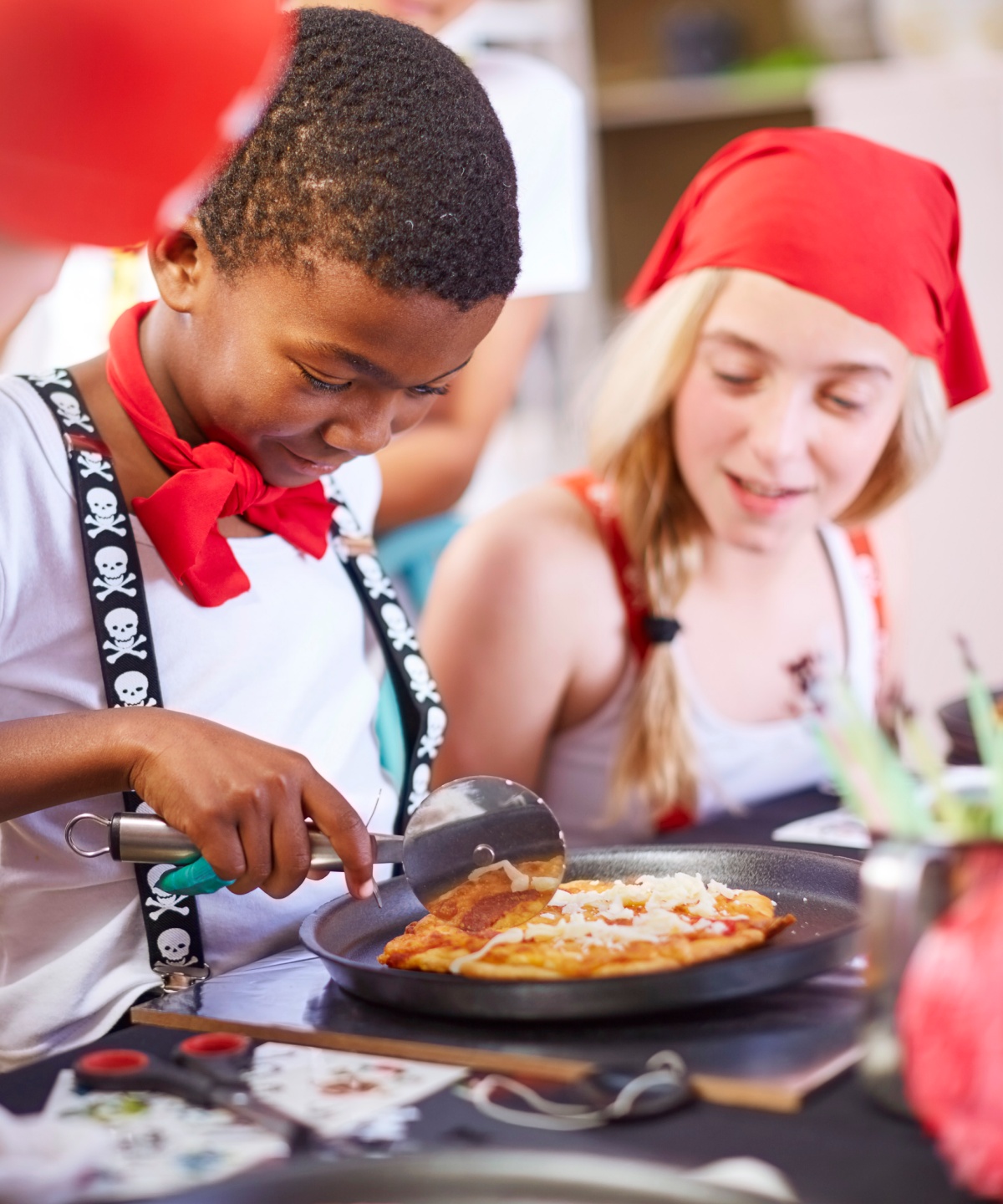 Verkleidete Kinder schneiden auf einem Kindergeburtstag eine Mini-Pizza.
