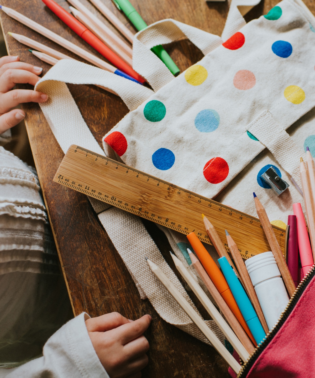 Schulutensilien wie Stifte, Lineal, Wasserflasche und gepunktete Tasche auf einem Tisch.