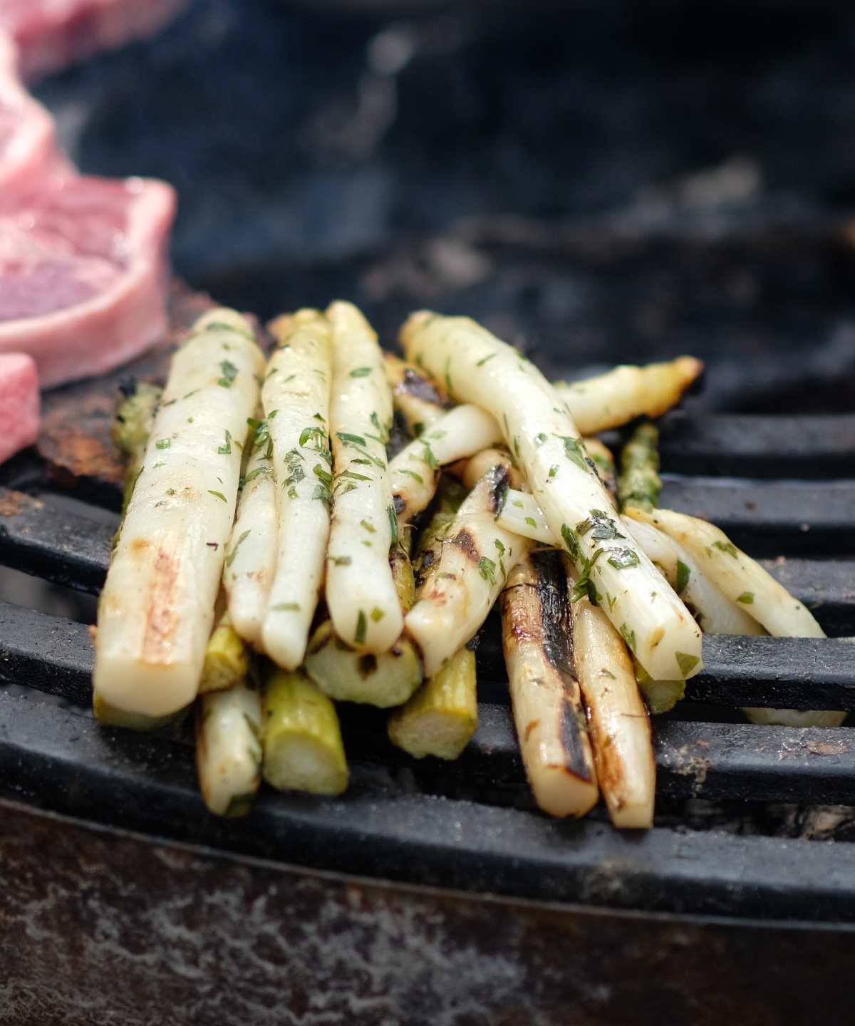 Weißer Spargel auf einem Grils, daneben noch ungegrillte Steaks.