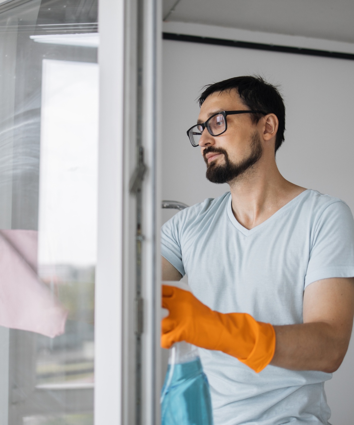 Mann mit Brille und Putzhandschuhen reinigt ein offenes Fenster mit einem Tuch.