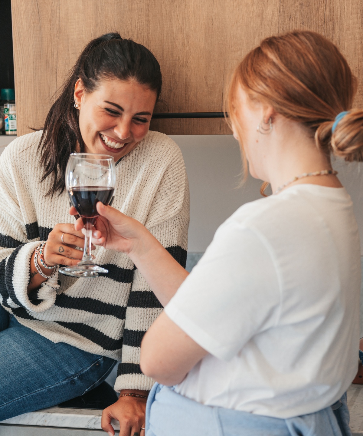 Zwei Frauen in einer Küche stoßen lächelnd mit Rotweingläsern an.