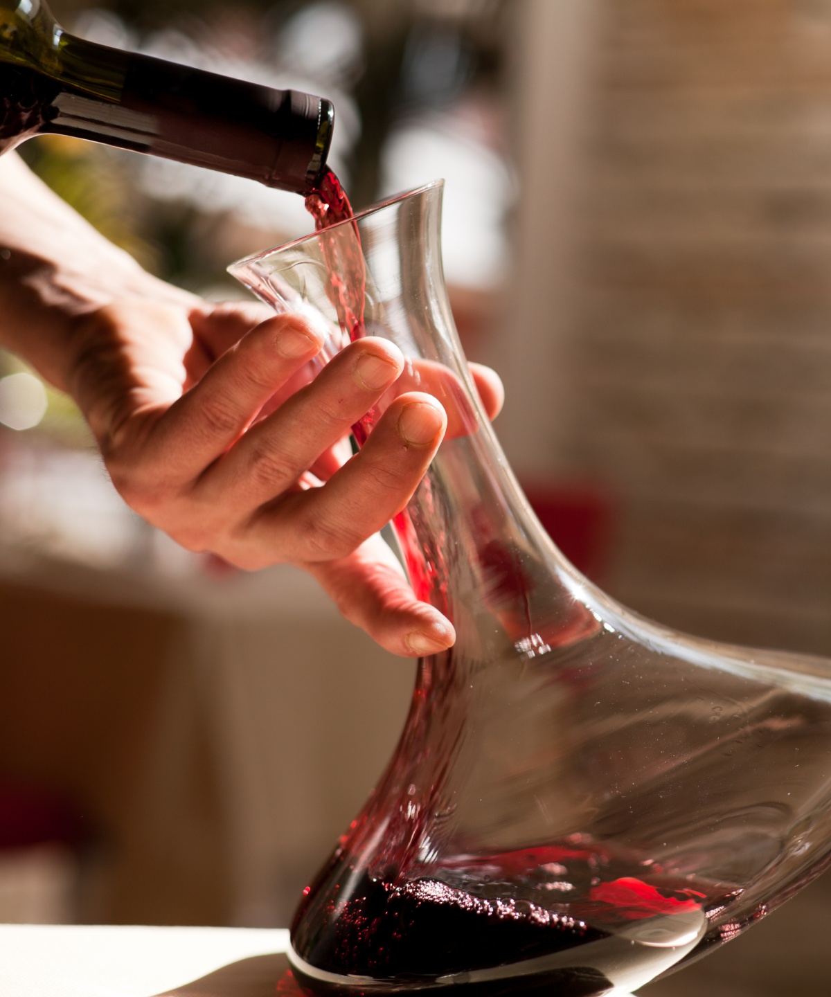 Person gießt Rotwein vorsichtig in einen Dekanter.