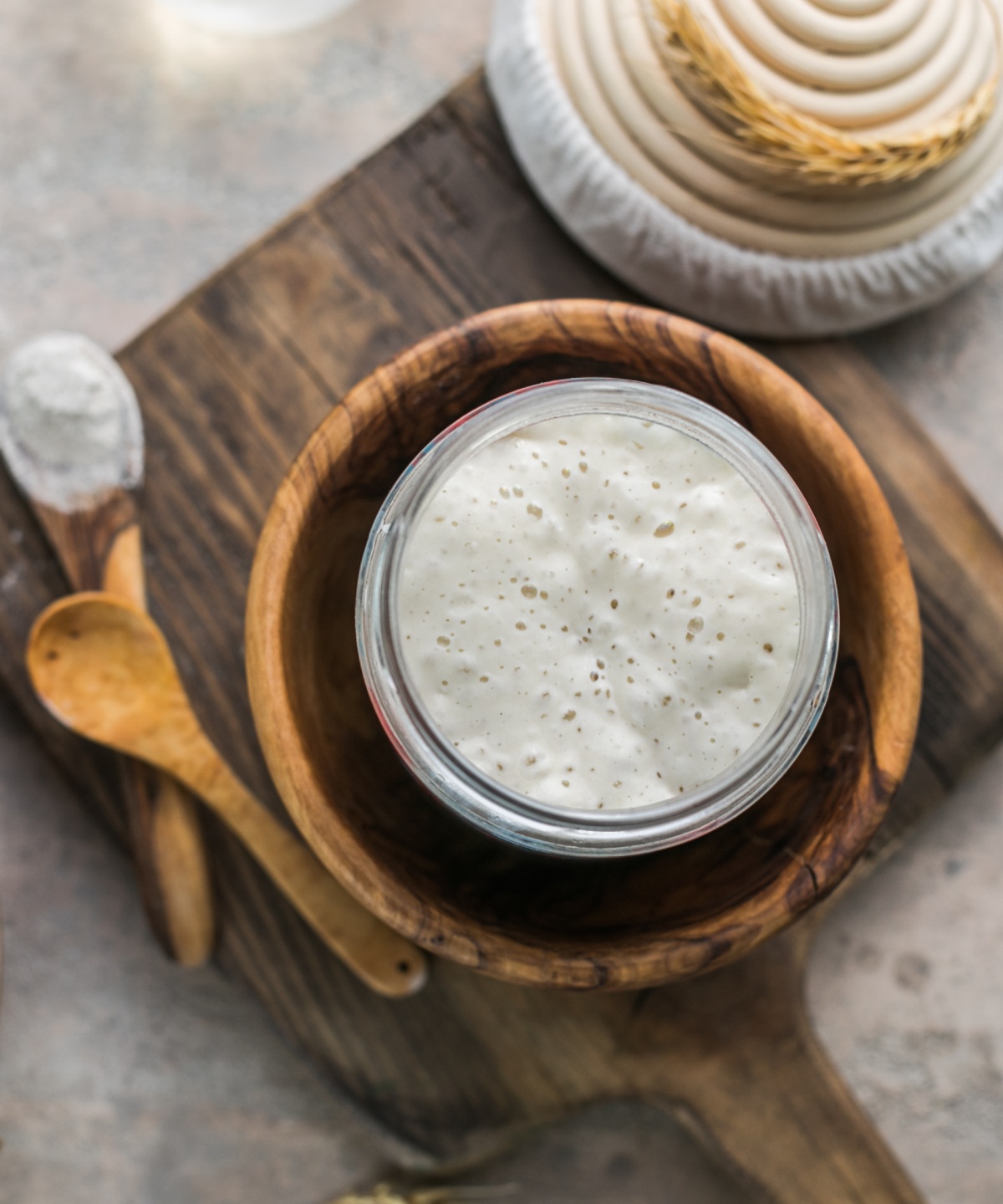 Ein Glas mit angesetztem Sauerteig, der Bläschen schlägt, auf einem Holzbrett.