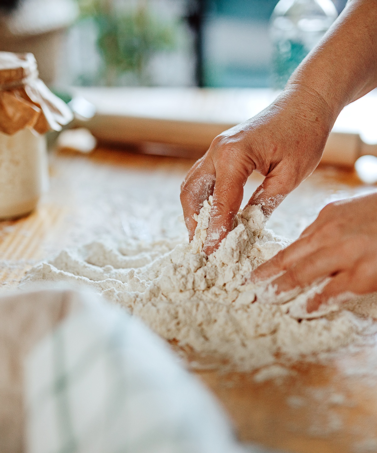 Person knetet Teig mit den Händen auf einer Holzunterlage.