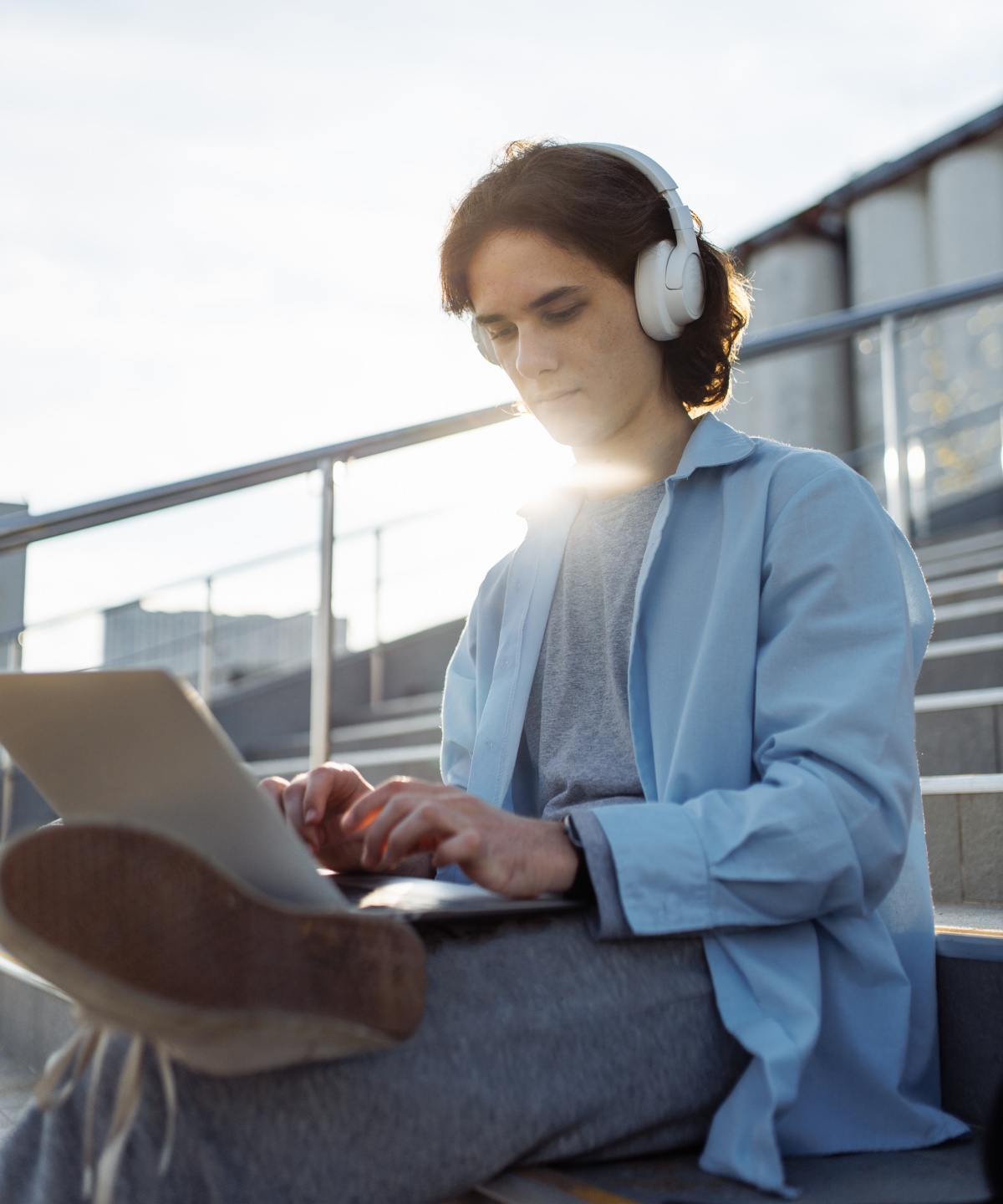 Person mit Kopfhörern shoppt oder arbeitet draußen am Laptop.