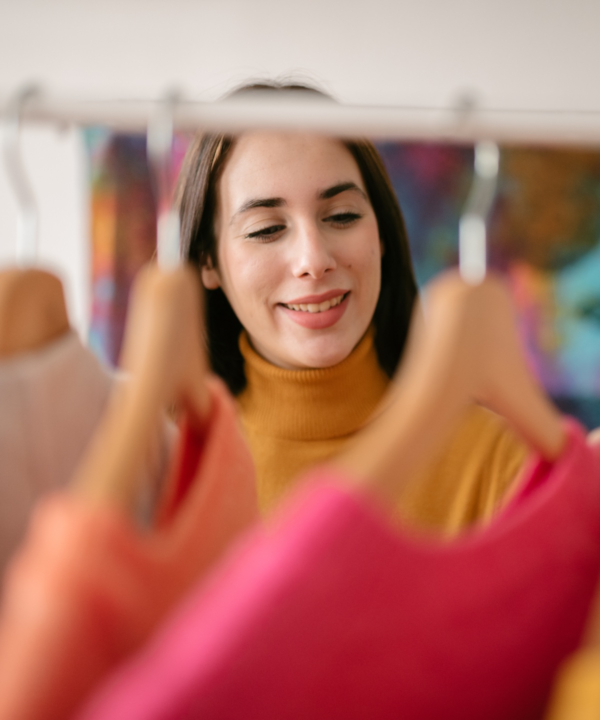 Frau schaut sich bunte Kleidung auf Kleiderbügeln an.