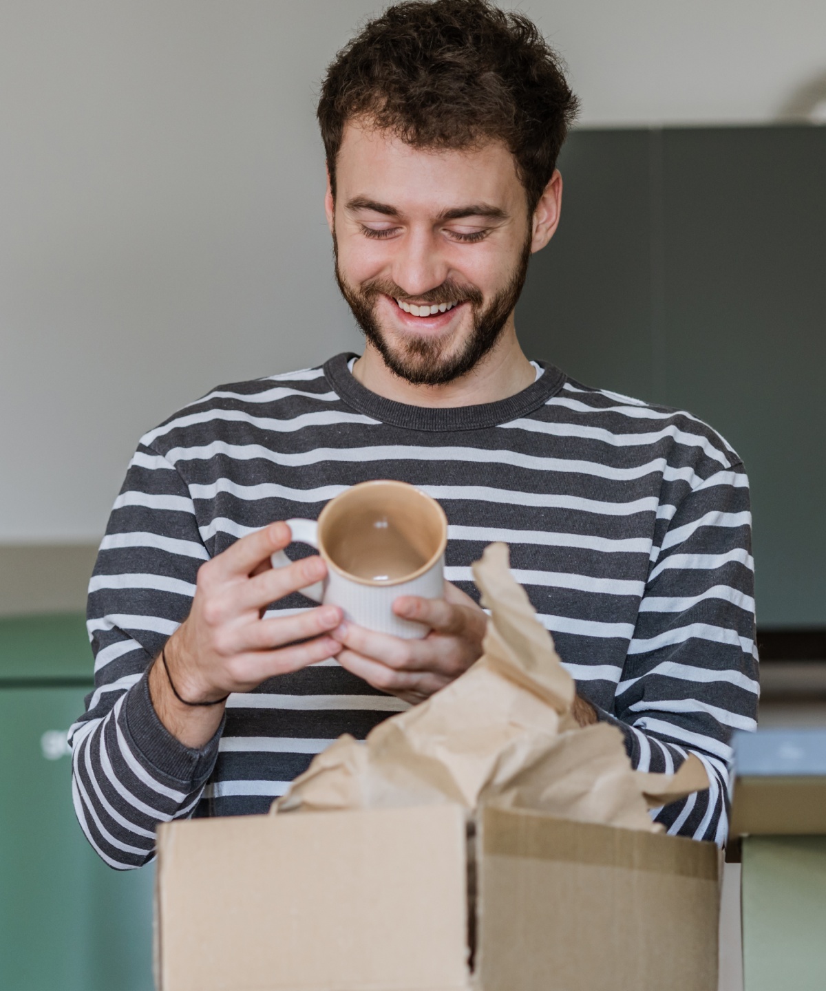 Mann packt eine Tasse aus einem Karton aus und lächelt.