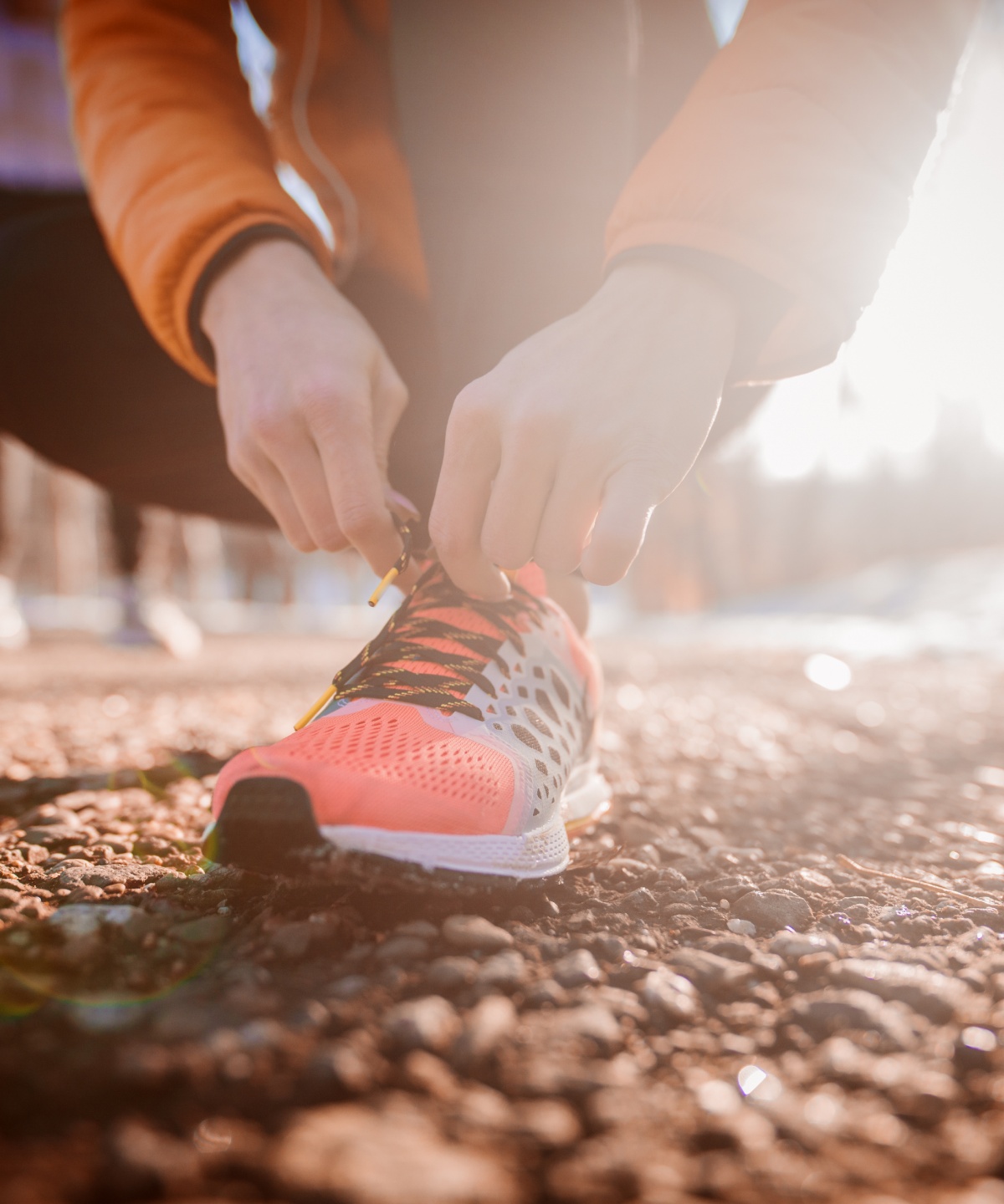 Person bindet sich orangefarbene Laufschuhe auf einem sonnigen Weg.
