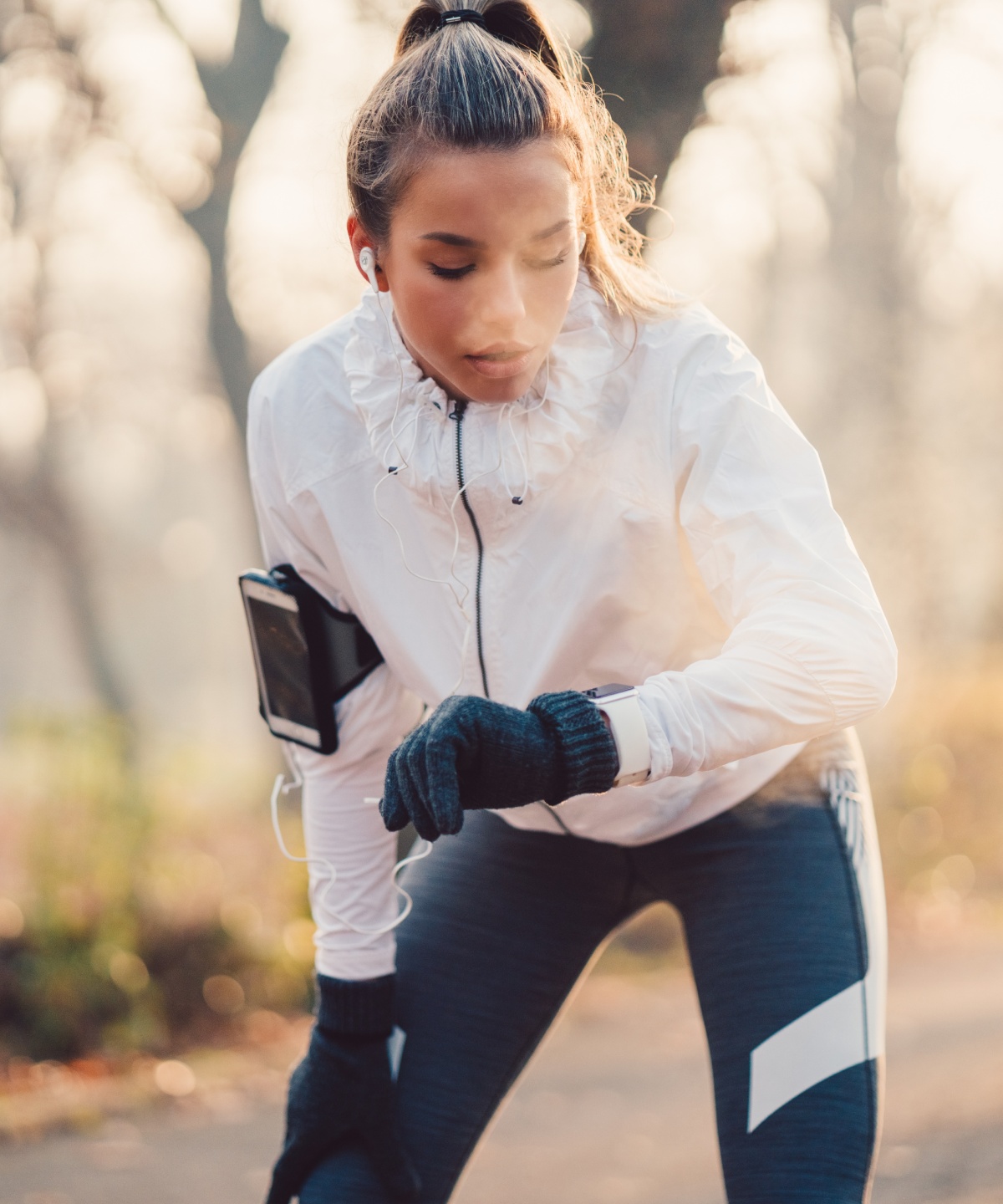 Frau in weißer Jacke überprüft ihre Smartwatch bei kurzer Pause während des Joggens im Park.