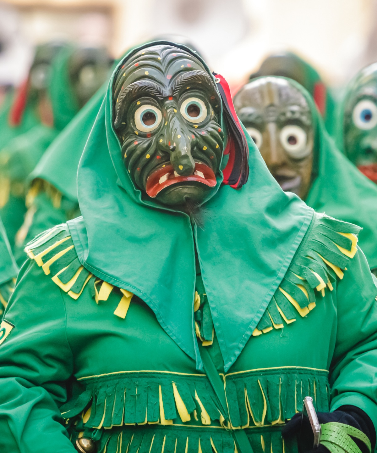 Gruppe von Personen in traditionellen, grünen geisterähnlichen Kostümen mit Holzmasken bei einem Karnevalsumzug.