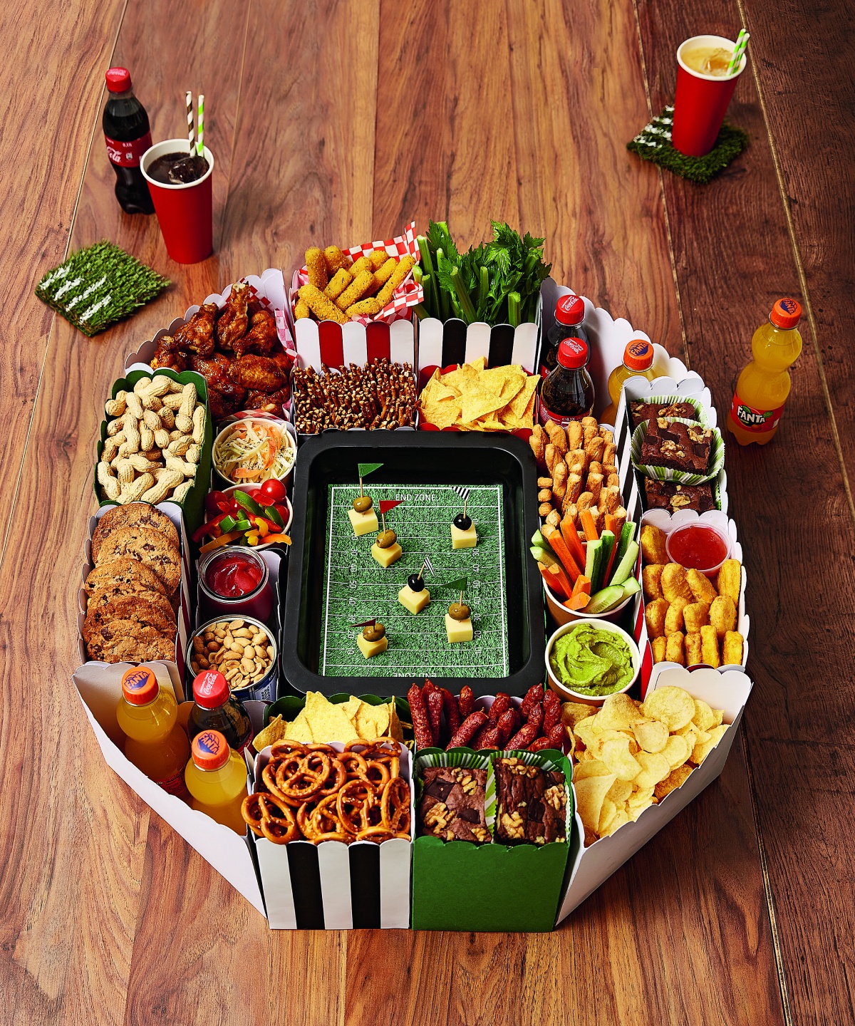 Aus bunter Pappe gebasteltes Snack-Stadion im American-Football-Design mit Chips, Gemüse, Dips, Brownies, Getränken und Fingerfood.