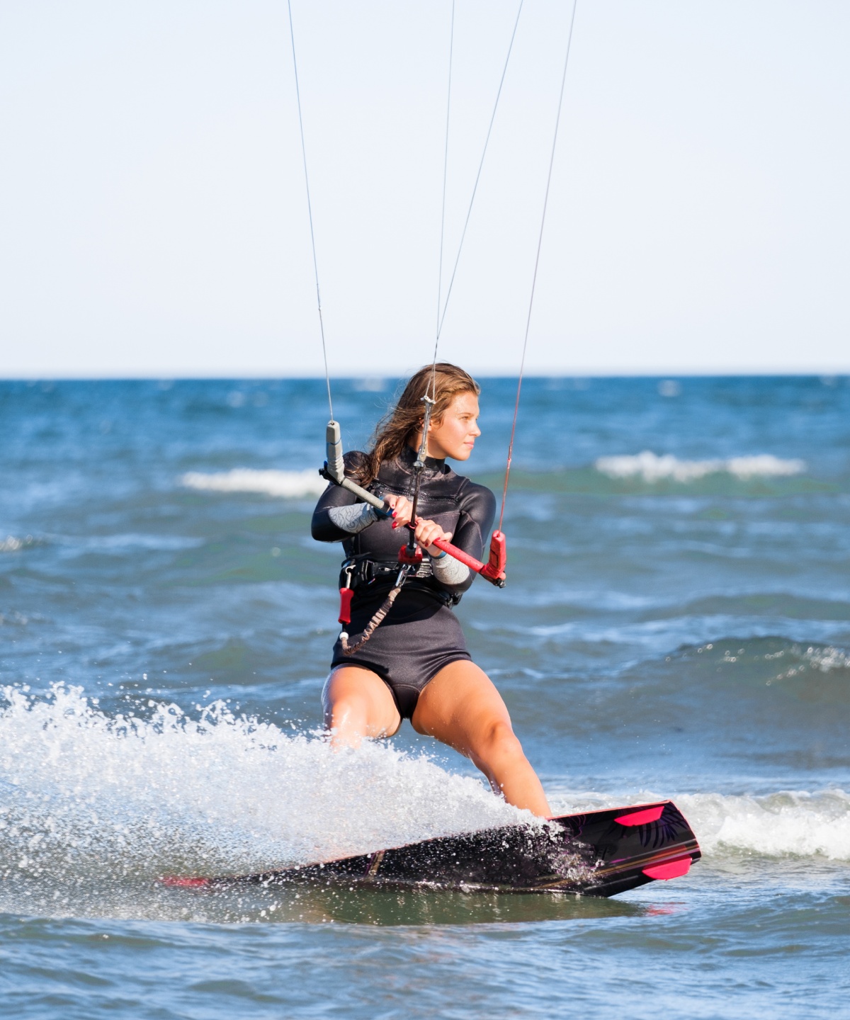 Frau in Neoprenanzug beim Kitesurfen auf dem Meer.