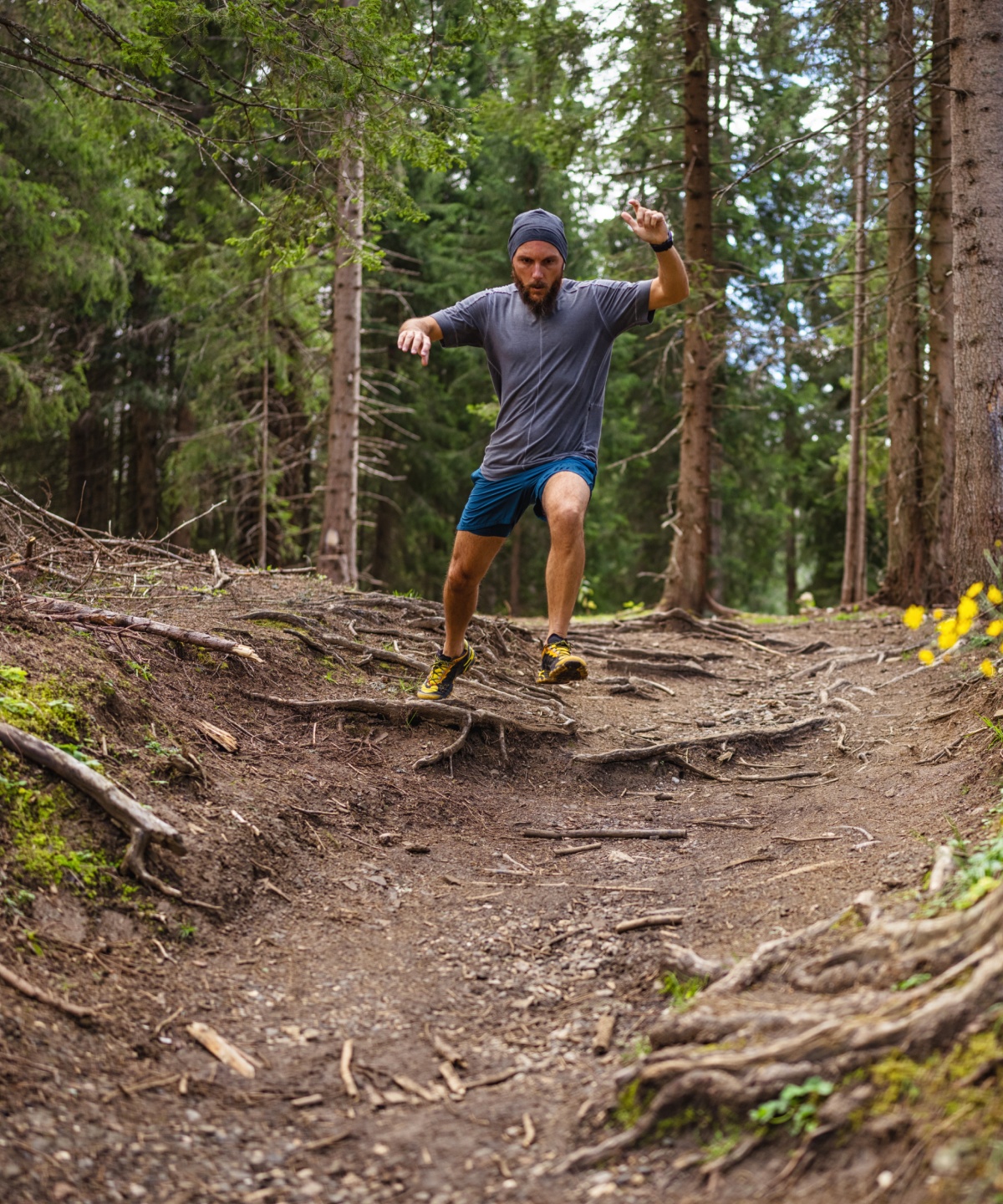 Mann joggt im Wald einen wurzeligen Hang entlang im Wald.