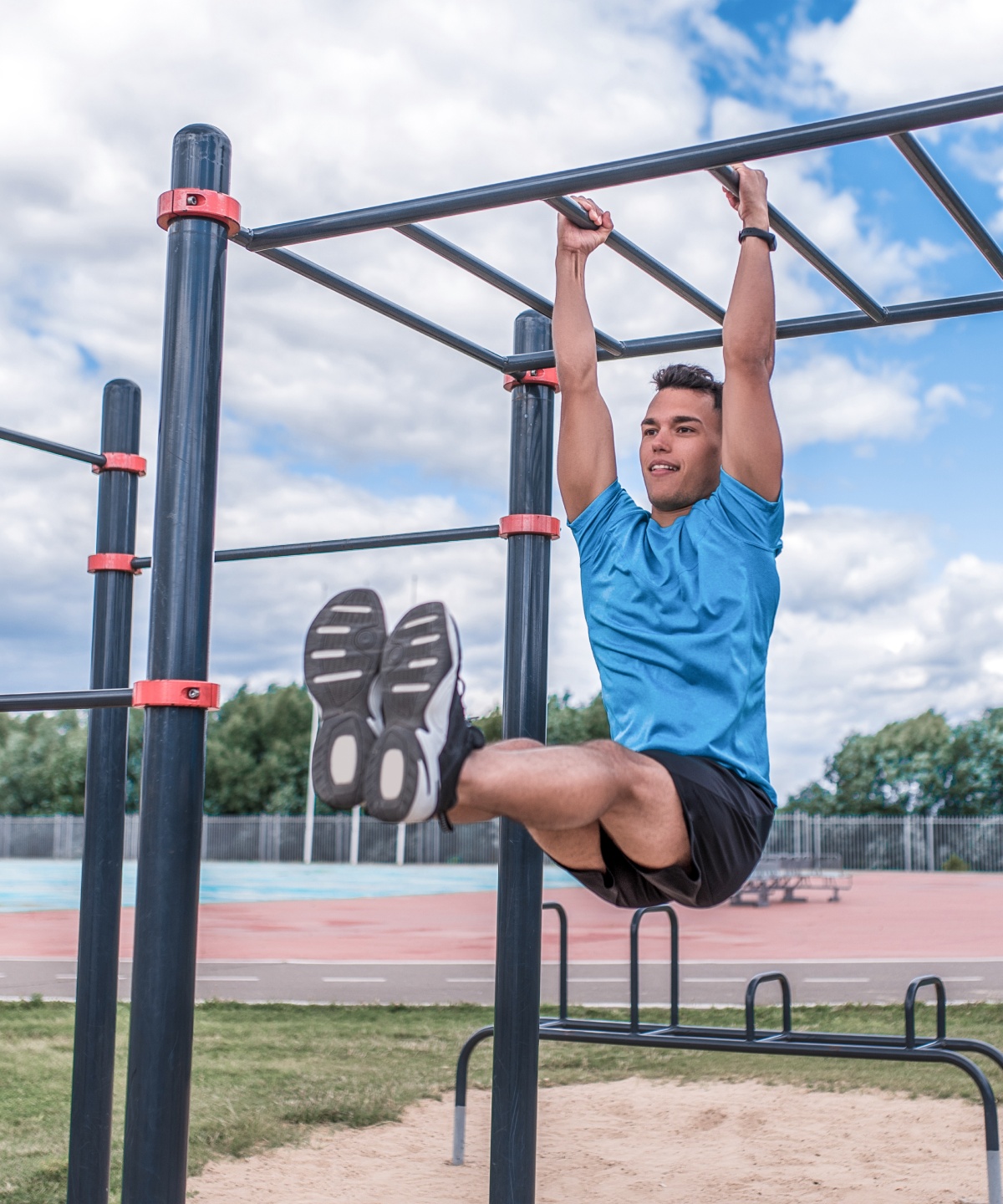 Mann in Sportkleidung macht Leg-Raises an einer Sprossenwand auf einem Sportplatz.