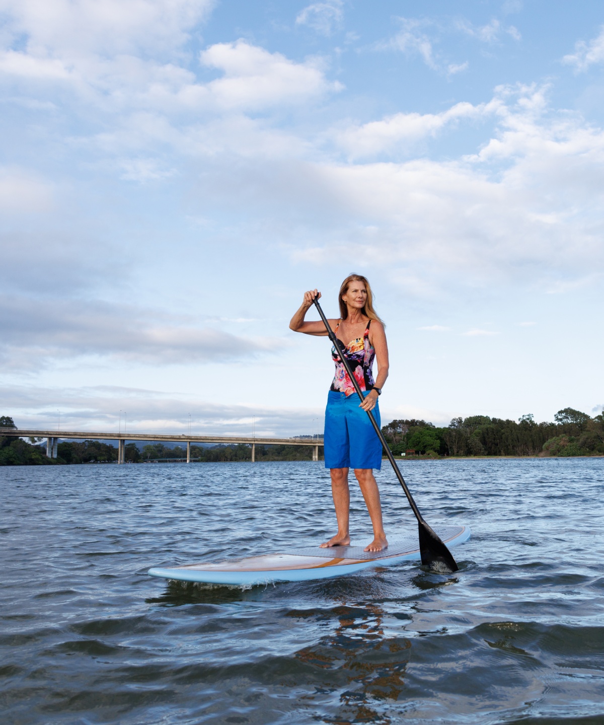 Frau in Badeanzug und Shorts macht Stand-Up-Paddling auf einem See
