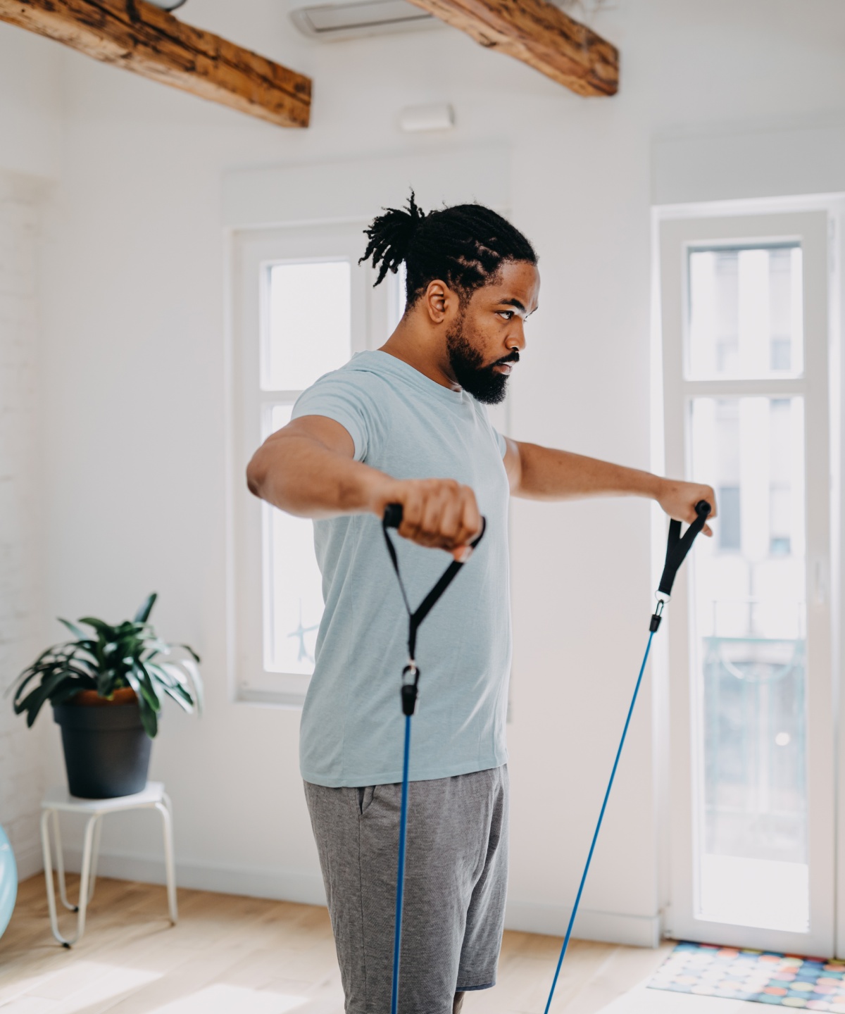 Mann trainiert mit Widerstandsband in hellem Raum vor weißer Backsteinwand.