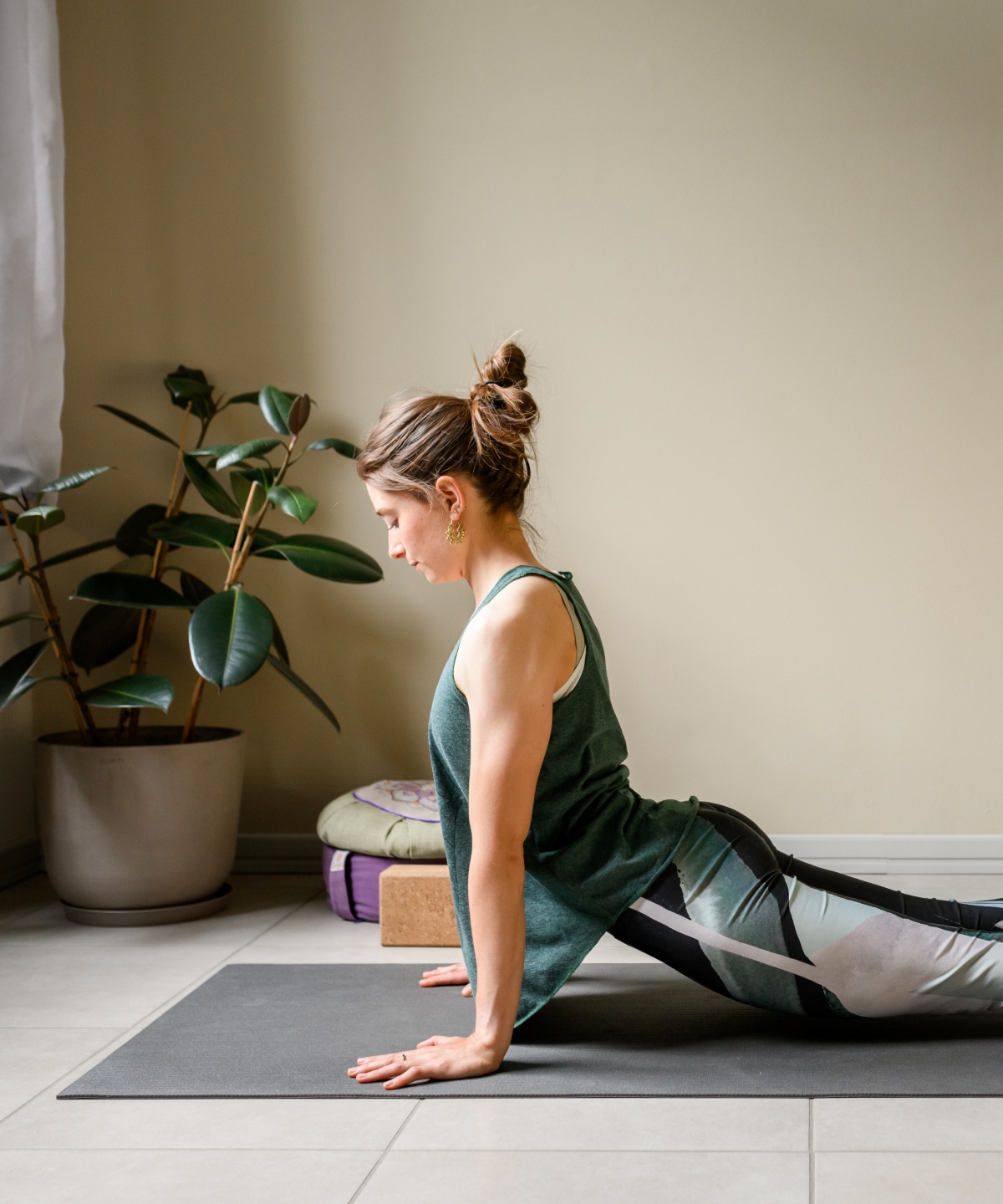 Frau macht Yoga-Kobra-Position auf grauer Matte in schlichtem Raum.
