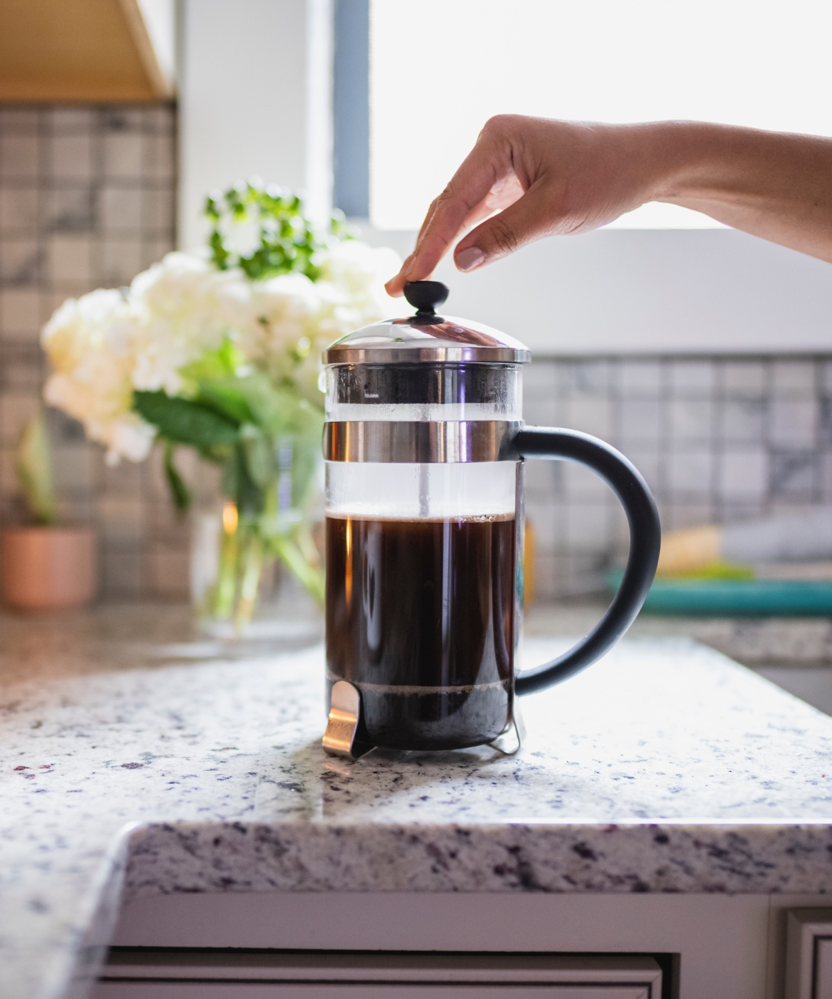 Eine Person drückt zum Kaffee kochen den Kolben einer French Press auf der Küchenarbeitsplatte.