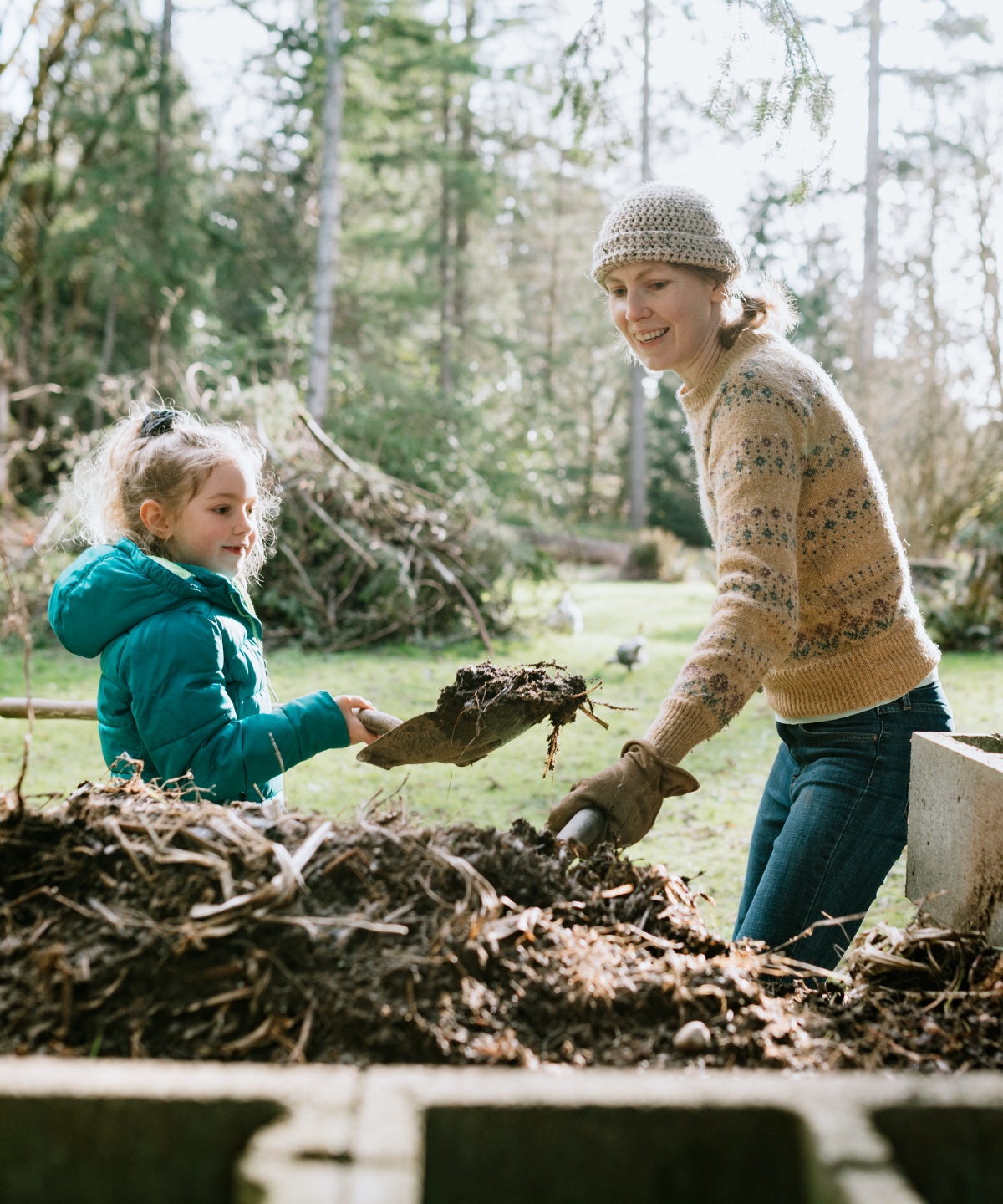 Frau und Kind im Grünen ernten mit Schaufeln Kompostgut.