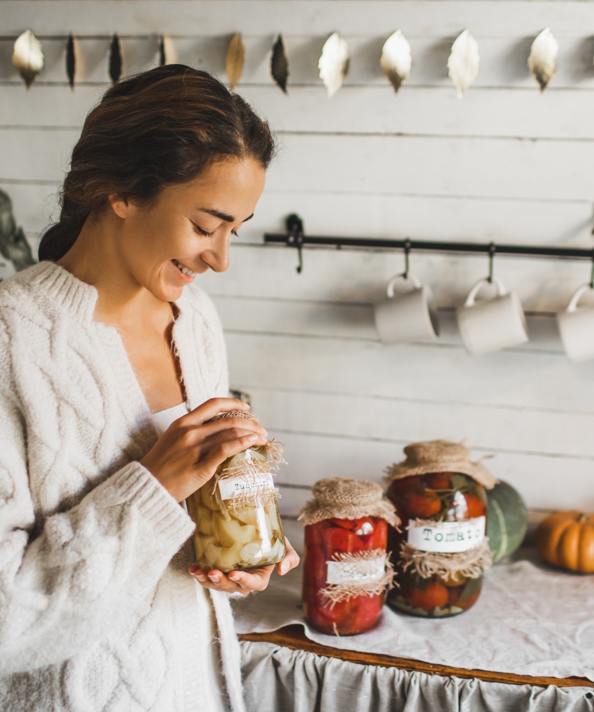 Eine junge Frau mit drei Gläsern eingelegter Lebensmittel.