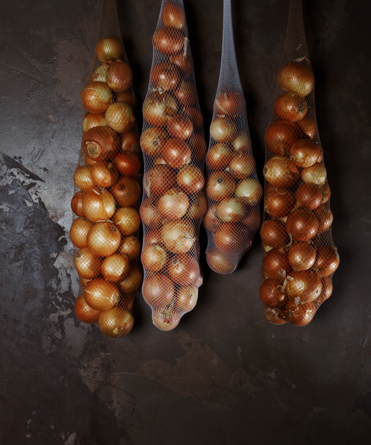 Zwiebeln im Vorratsnetz hängen in einem dunklen Raum.