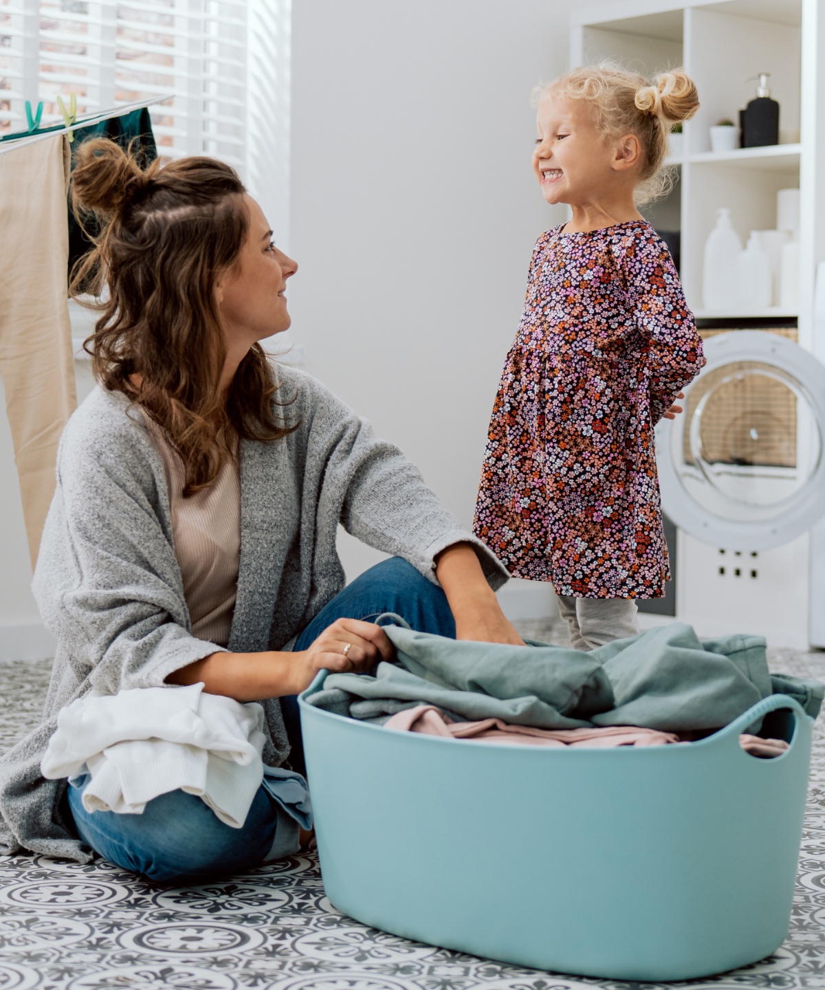 Eine Frau und ein Mädchen stehen an einem Korb voll Buntwäsche.