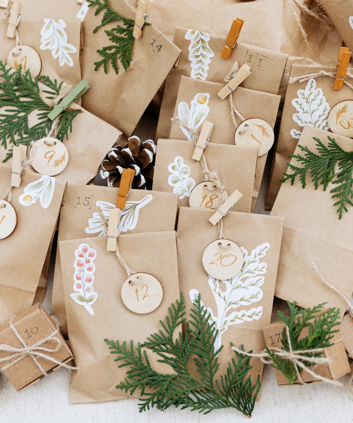 Adventskalender aus hellbraunen Papiertüten mit Holzanhängern und grünen Zweigen.