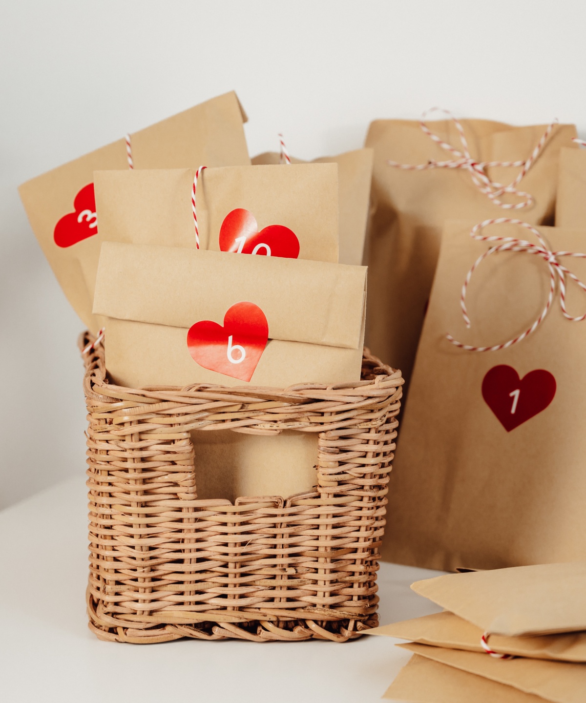 Adventskalender aus befüllte Papiertüten mit Herzverzierung stehen in einem Bastkorb.