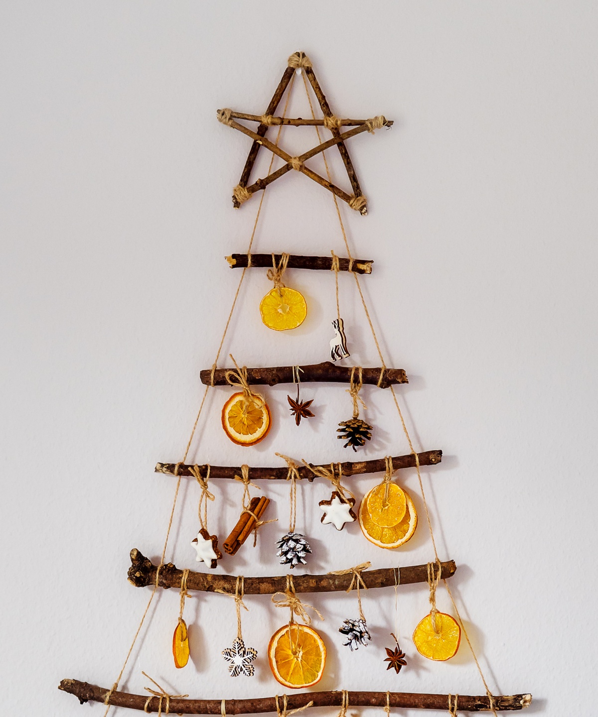 Weihnachtsbaum-Wanddekoration aus Ästen, mit getrockneten Orangenscheiben, Sternanis und Tannenzapfen verziert.