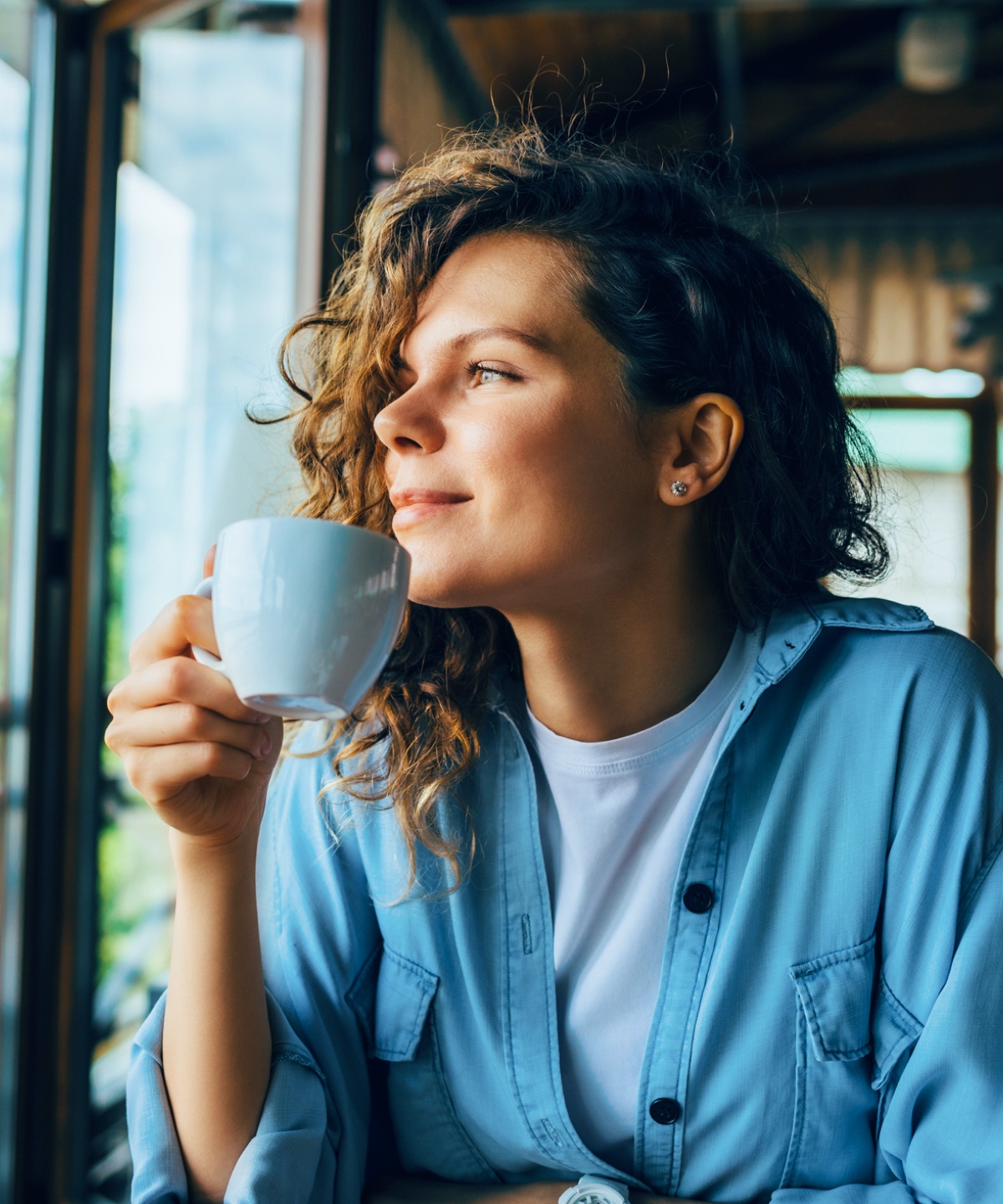 Frau mit Teetasse in der Hand schaut zufrieden aus dem Fenster