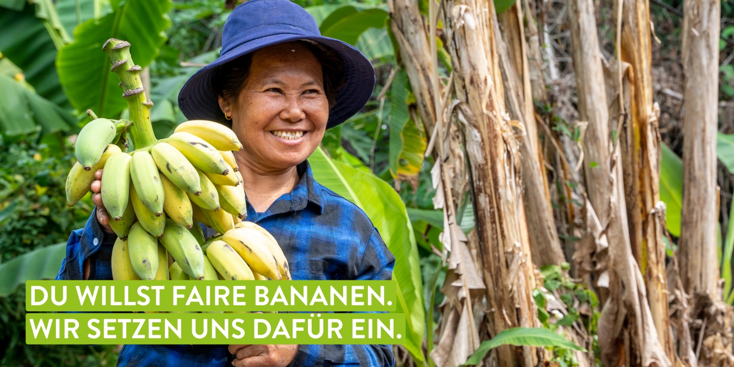 Lachende Landwirtin präsentiert große Staude grüner Bananen vor tropischem Hintergrund auf einer üppigen Plantage.