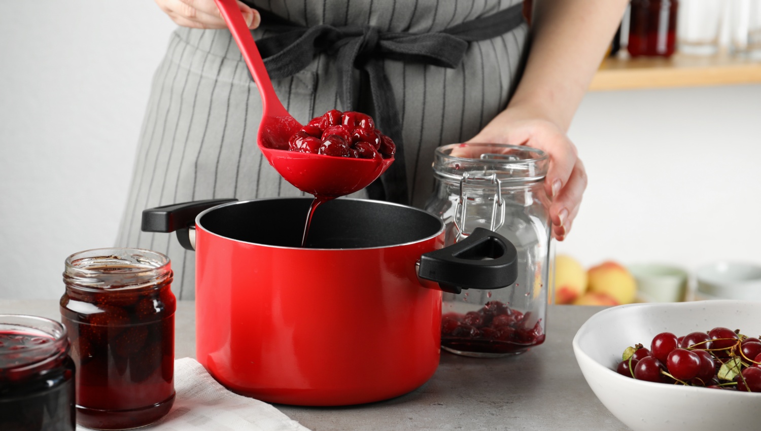 Person füllt Kirschkompott mit einer Kelle in ein Glas zur Vorbereitung für das Einkochen im Backofen.