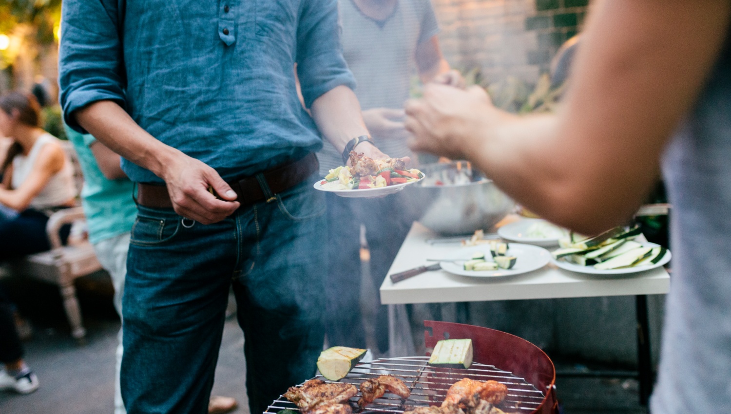 Partygäste holen sich mariniertes Fleisch und Gemüse vom Grill.