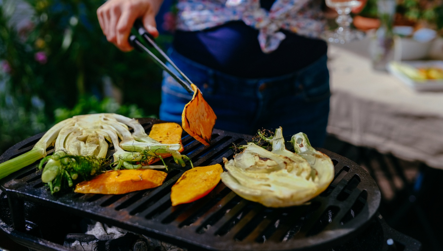 Person grillt Gemüse wie Kürbis und Fenchel auf einem Grill.