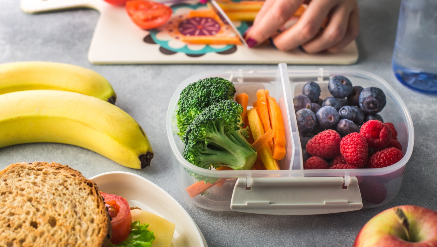 Jemand bereitet eine Brotdose aus Obst und Gemüse vor.