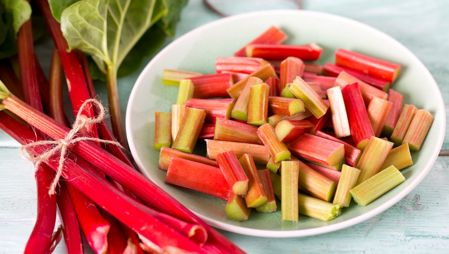 Zum Einfrieren vorbereiteter Rhabarber in Stücke geschnitten, daneben frische Rhabarberstangen.