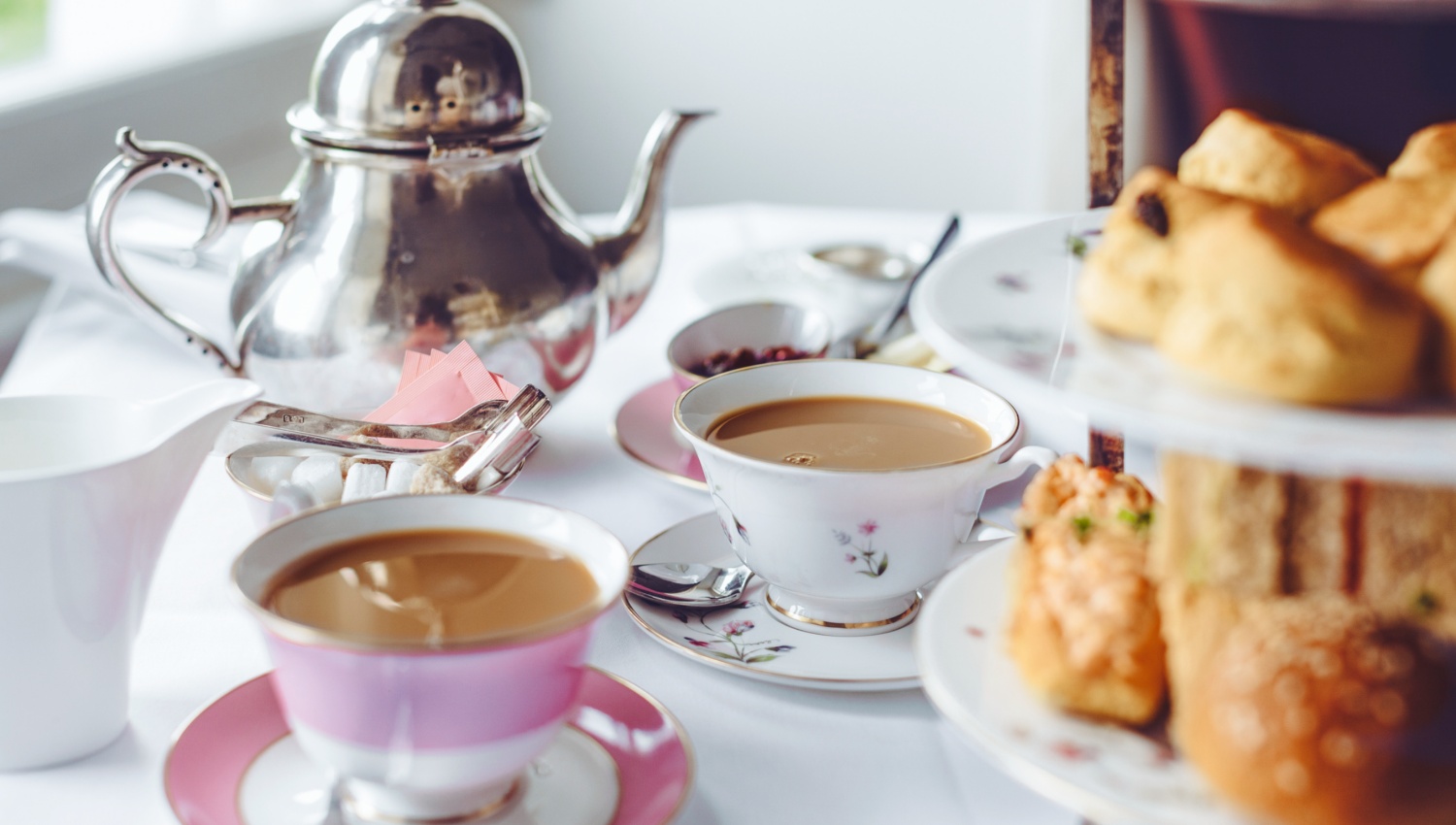 Eine Etagere mit Scones, Tassen mit Milchtee und eine schicke Silberkanne