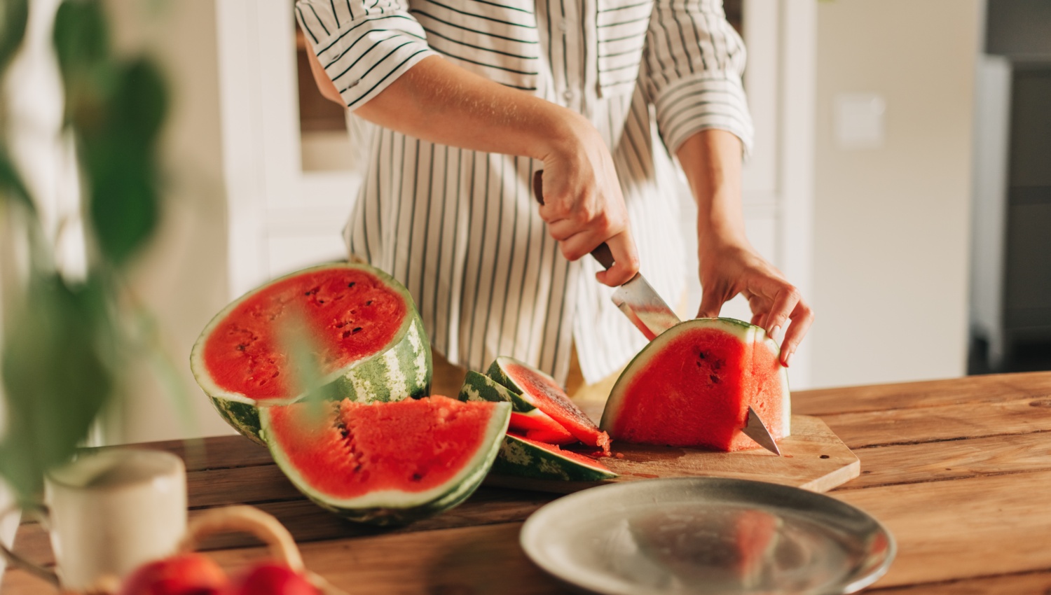 Eine Person schneidet eine reife Wassermelone auf einem Küchenbrett in Scheiben