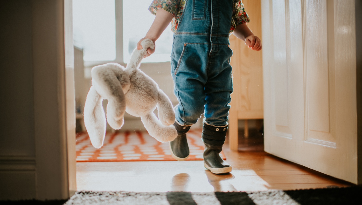 Eine Kleinkind läuft mit seinem Kuscheltier durch das Haus.