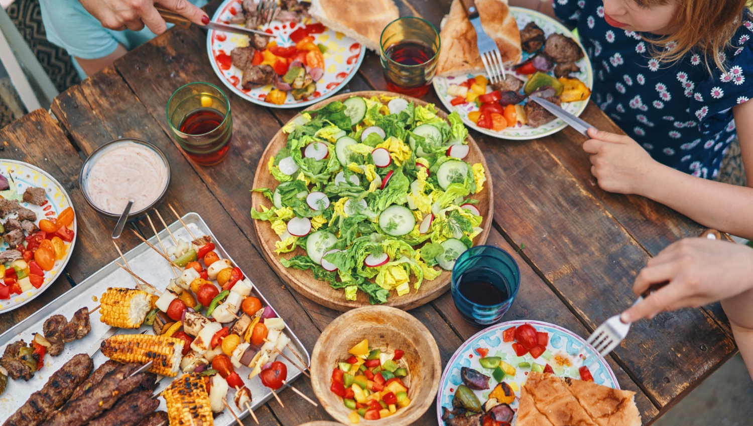 Familie beim Grillen, es gibt buntes Grillgemüse, Salat und gegrilltes Fleisch.