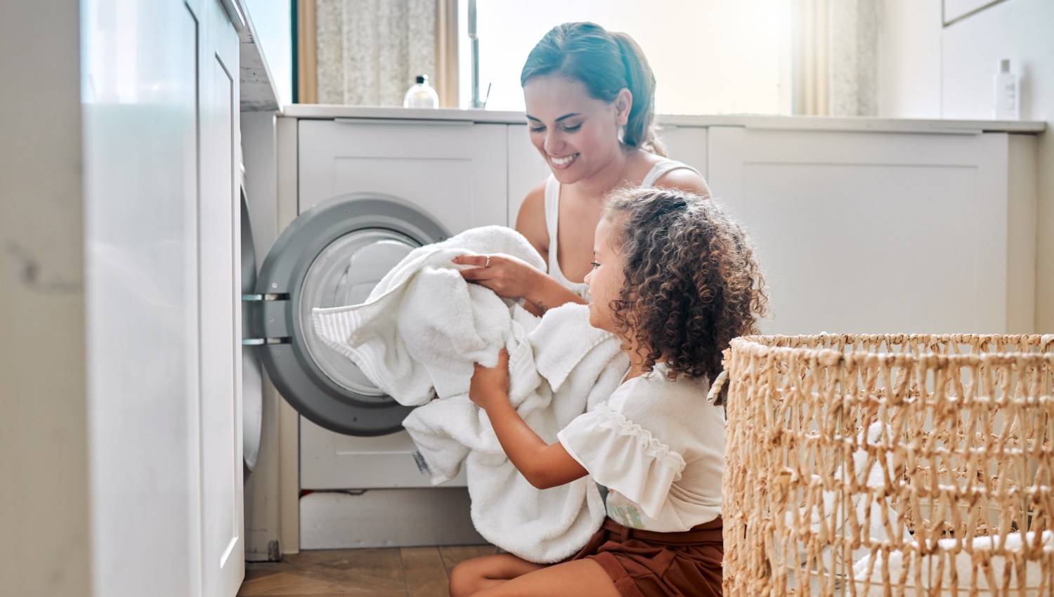 Eine Frau und ein Mädchen räumen gemeinsam weiße Wäsche in die Waschmaschine.