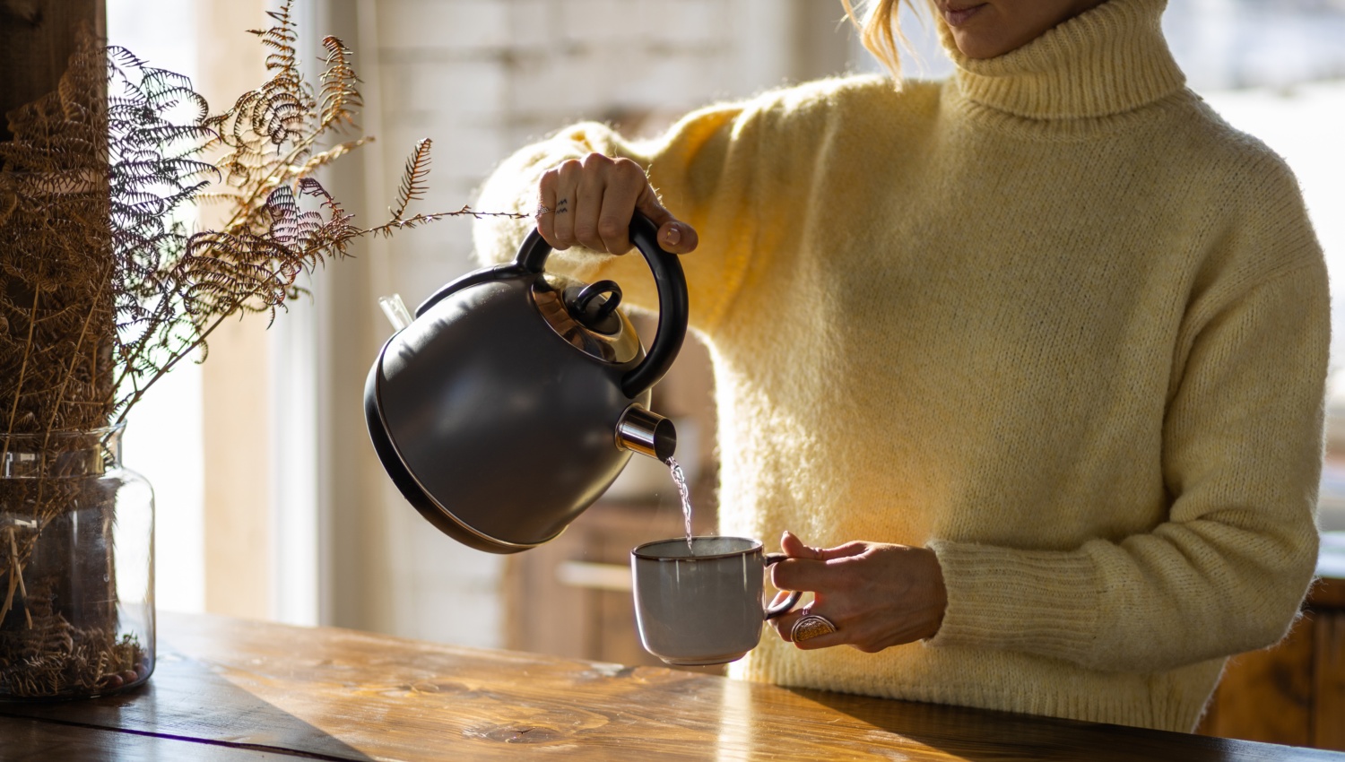 Eine Frau schenkt sich heißes Wasser in eine Tasse.