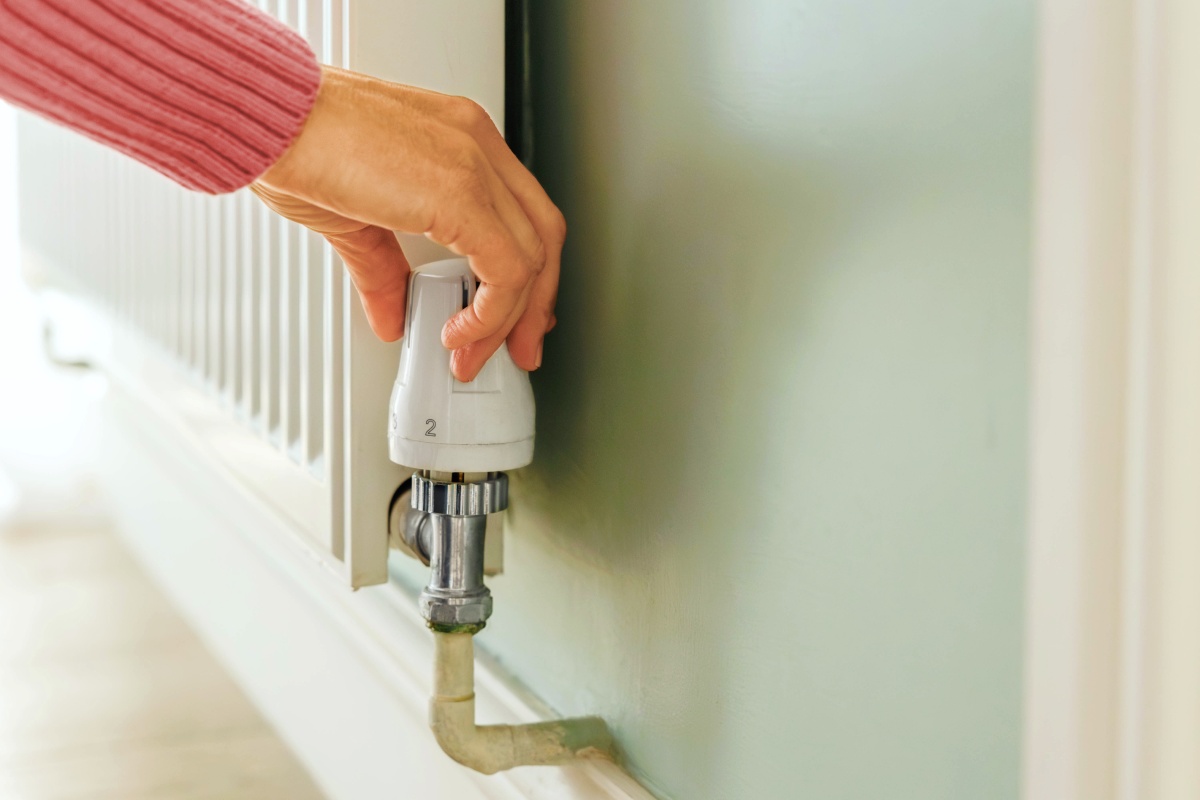 Eine Person stellt die Temperatur an der Heizung ein.