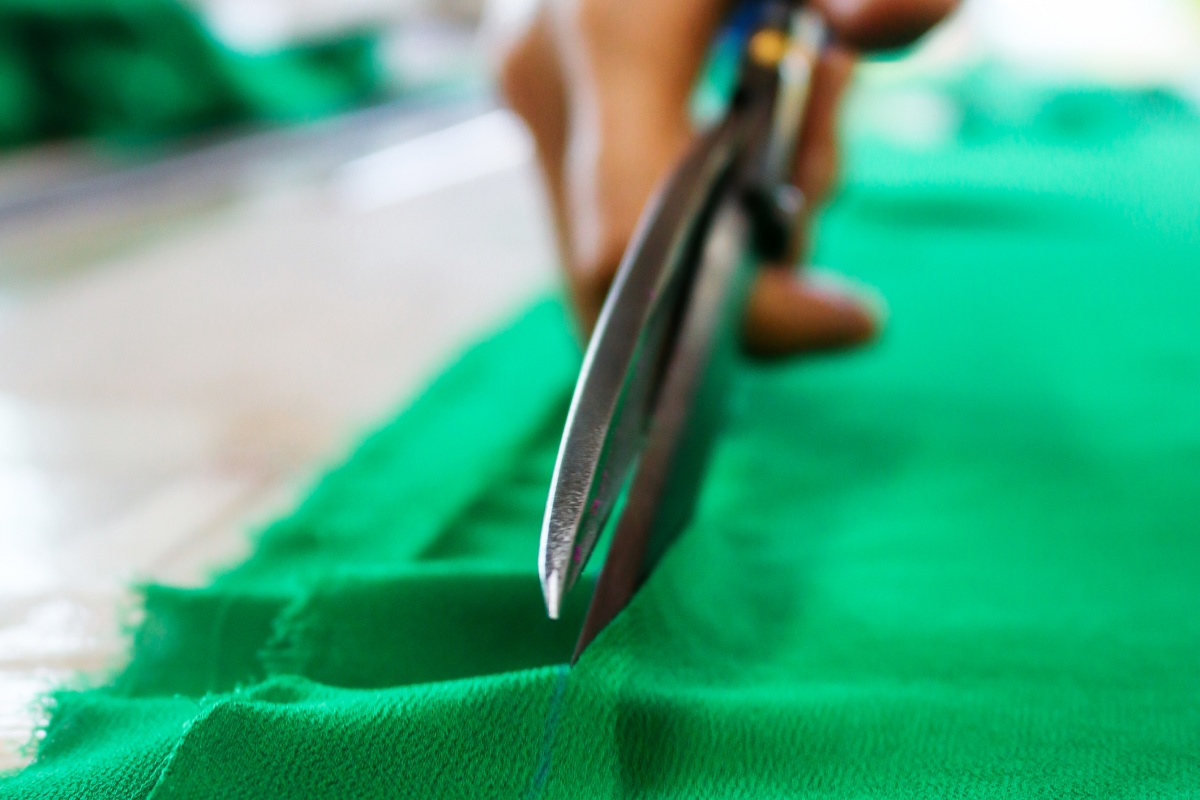 Eine Hand schneidet durch grünen Stoff.